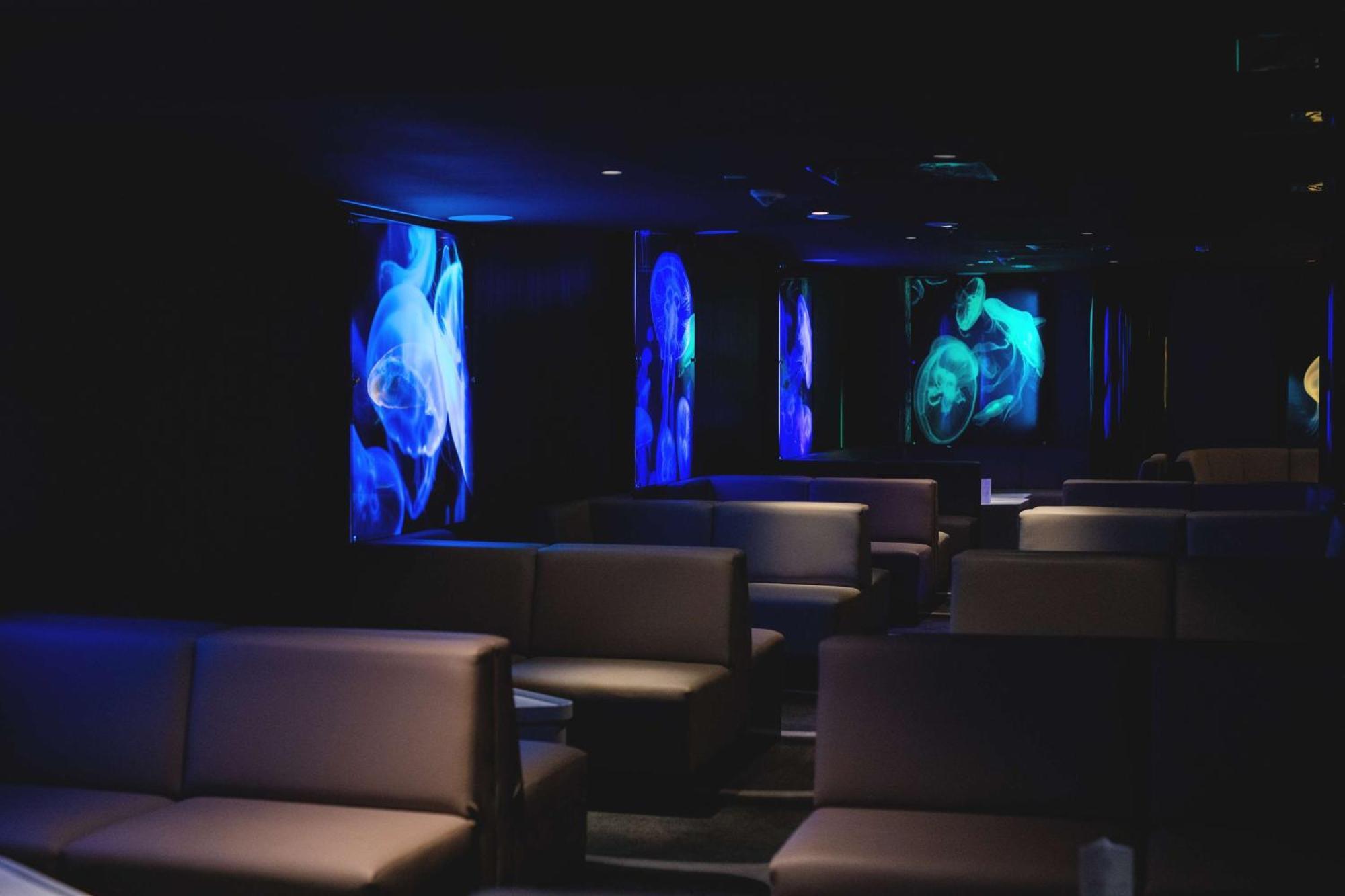 Radisson Blu Resort Swinoujscie Kültér fotó The photo shows a dimly lit interior space, likely a lounge or a seating area. The walls are adorned with glowing blue and turquoise images, possibly of jellyfish or abstract aquatic forms, creating an ambient atmosphere. There are several upholstere