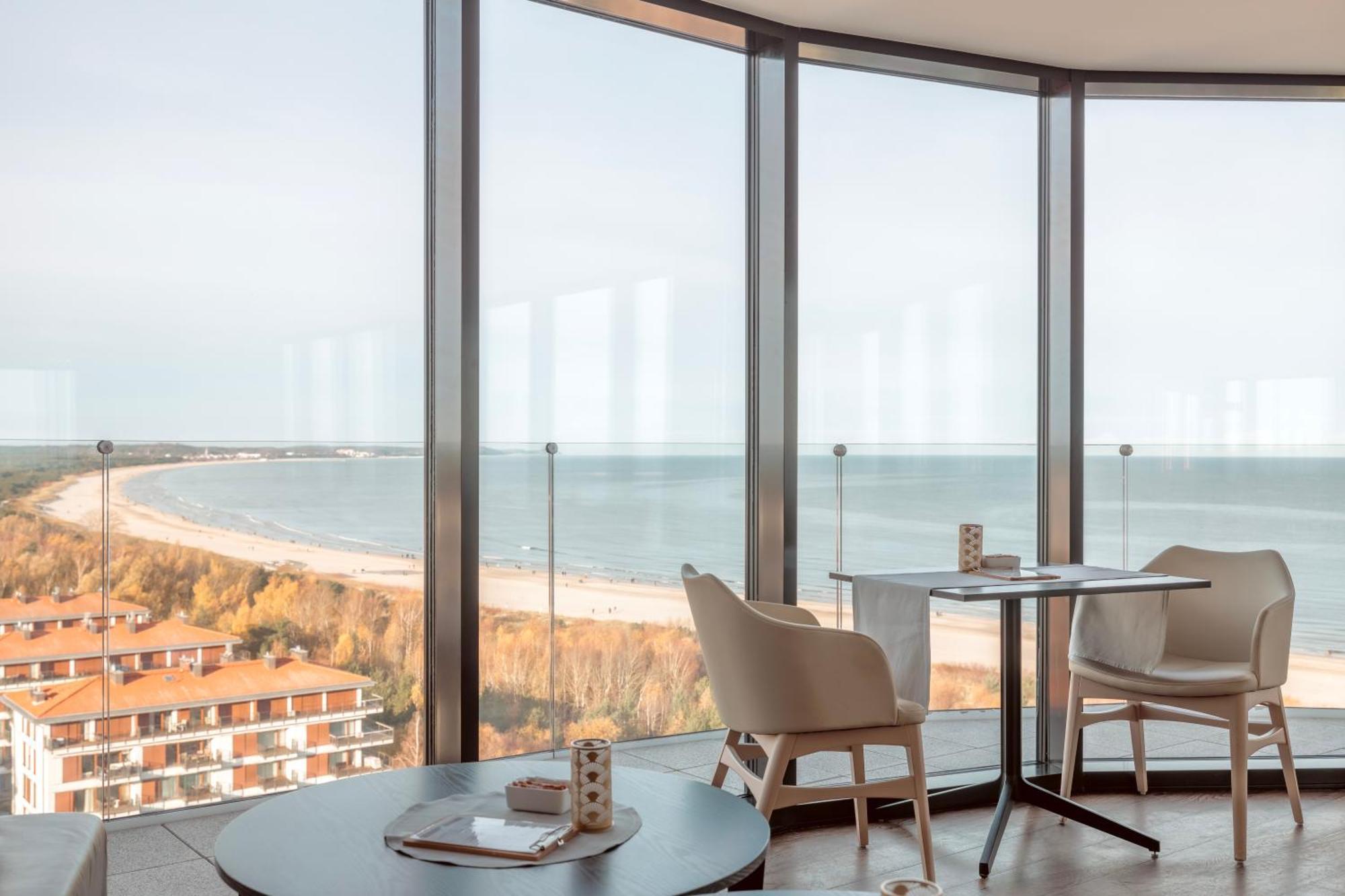 Radisson Blu Resort Swinoujscie Kültér fotó The photo shows a modern interior space with large floor-to-ceiling windows that provide a stunning view of the beach and sea. The area appears to be a dining or lounge space, featuring a minimalistic table and chairs. There is a sense of tranquility