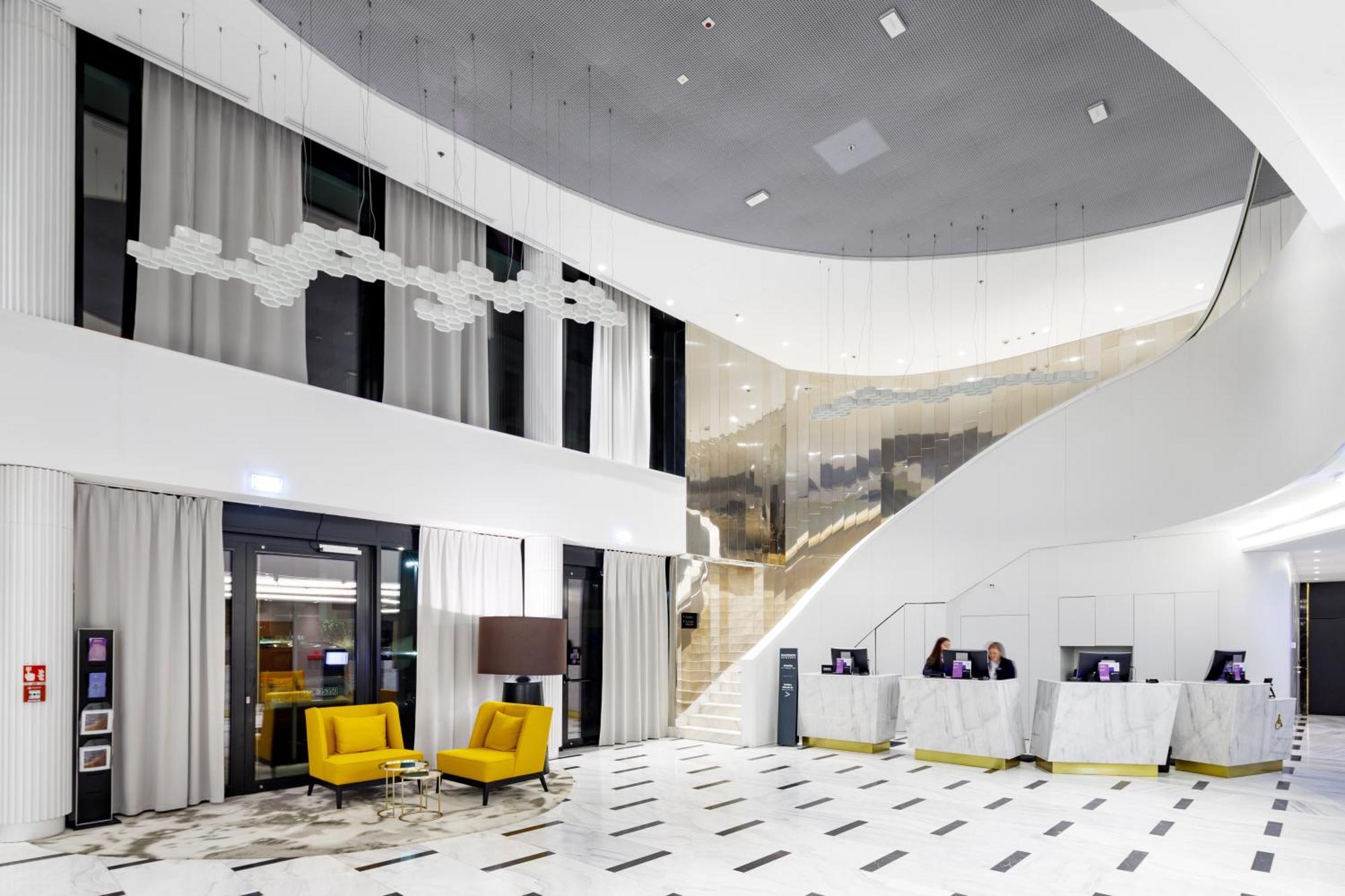 Radisson Blu Resort Swinoujscie Kültér fotó The photo shows a modern interior space, likely a hotel or a lobby area. It features a spacious, open design with high ceilings and a stylish staircase that leads to an upper level. The walls are mostly white, with large windows allowing natural ligh