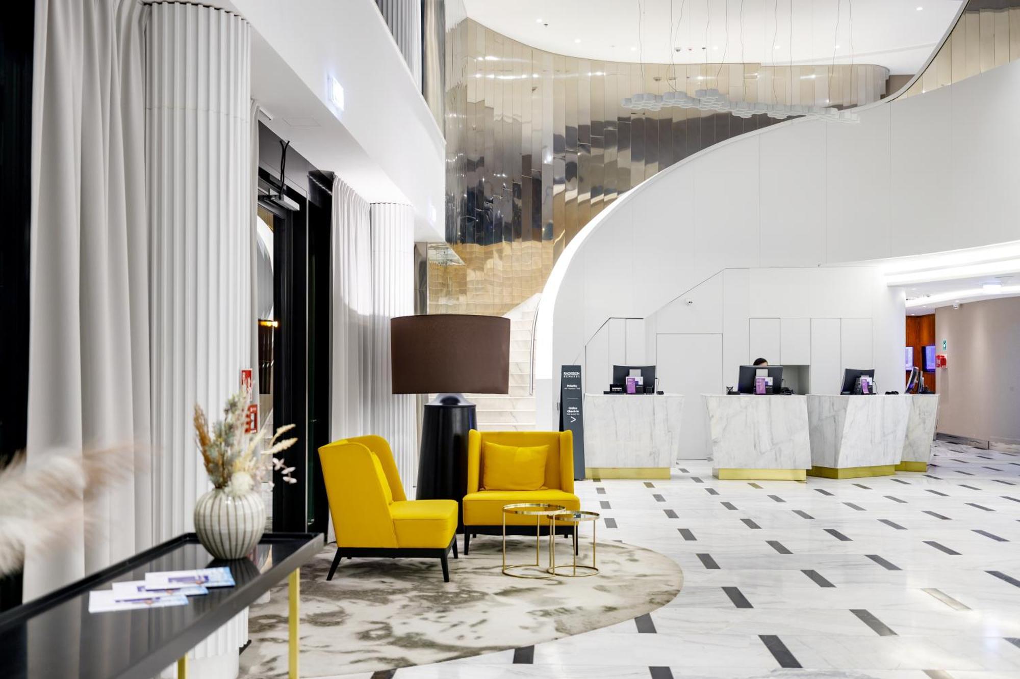 Radisson Blu Resort Swinoujscie Kültér fotó The photo shows the interior of a modern hotel lobby. The space features a stylish design with a combination of yellow and neutral-colored seating, including two yellow armchairs and a small table. In the background, there is a reception area with ma