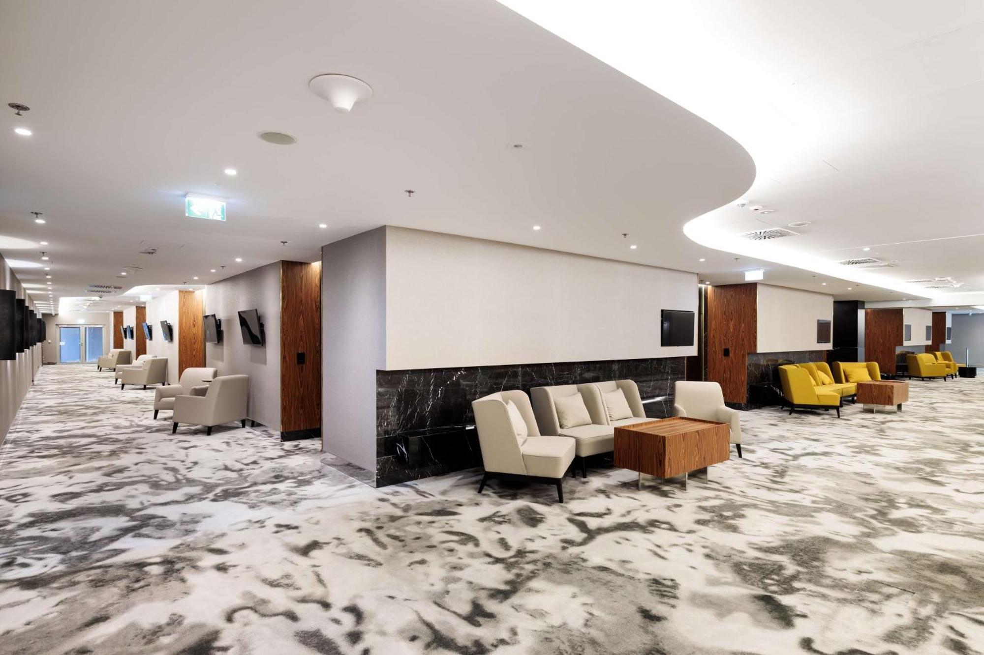 Radisson Blu Resort Swinoujscie Kültér fotó The photo shows a modern interior space, likely a lobby or lounge area. The flooring features a patterned carpet, and the walls are neutral in color, creating a calm ambiance. There are comfortable seating arrangements, including a group of beige cha