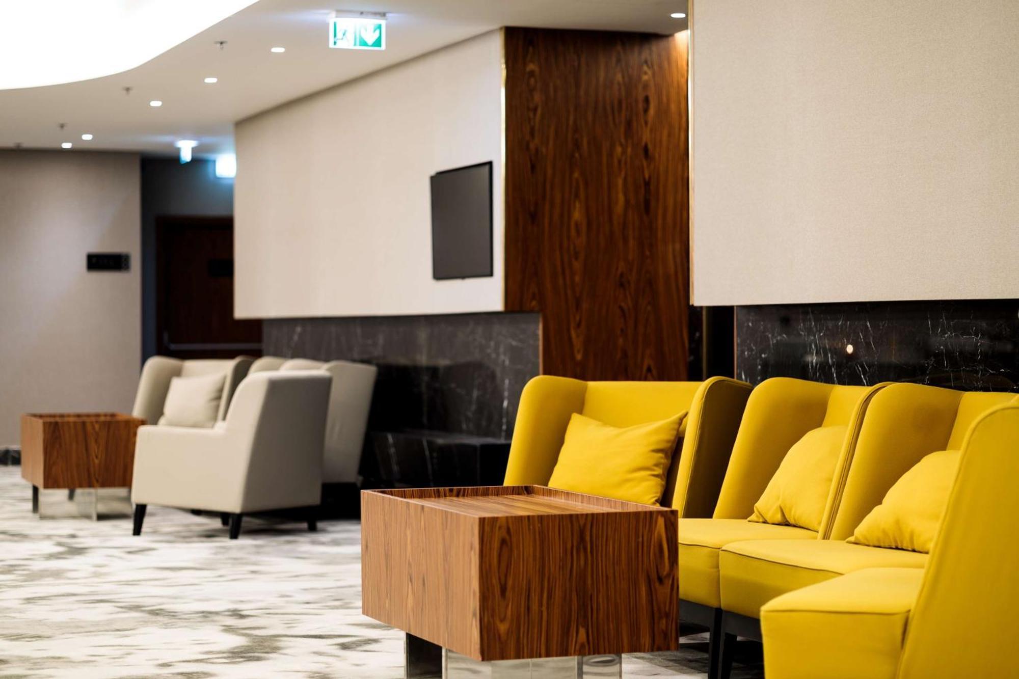 Radisson Blu Resort Swinoujscie Kültér fotó The photo depicts a modern lounge or waiting area with stylish seating. On the left, there are soft gray armchairs arranged around a wooden coffee table. In the center, there are yellow chairs with plush cushions, contributing a vibrant contrast to t