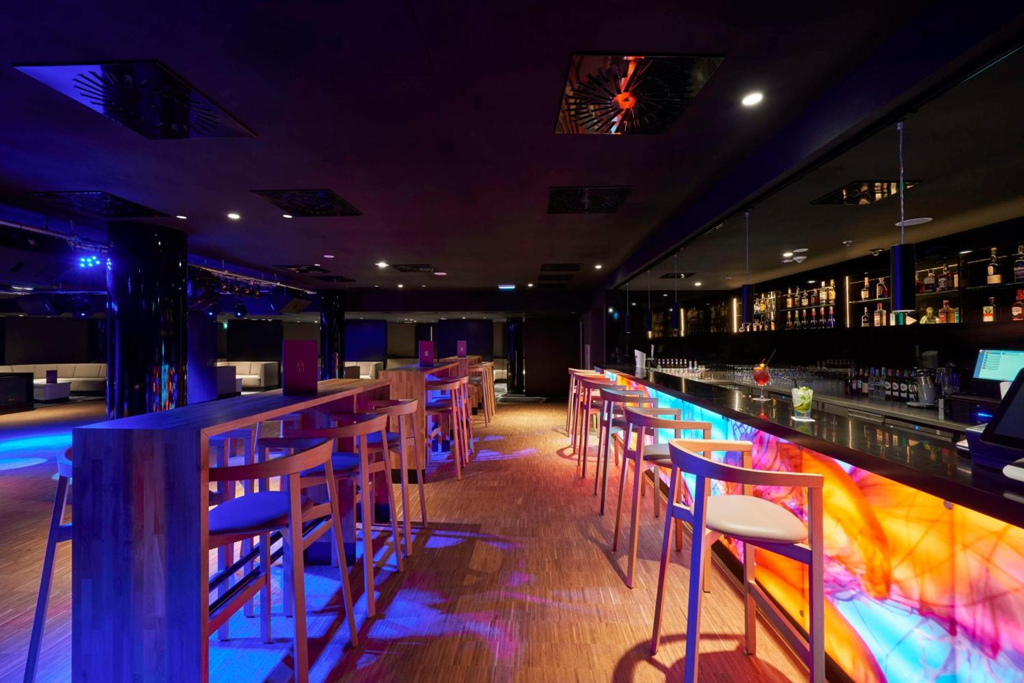 Radisson Blu Resort Swinoujscie Kültér fotó The photo depicts a modern bar interior with a sleek and contemporary design. There are high wooden stools positioned along a bar counter, which features vibrant, colorful lighting underneath. The bar area is dimly lit, creating a nightlife ambiance,