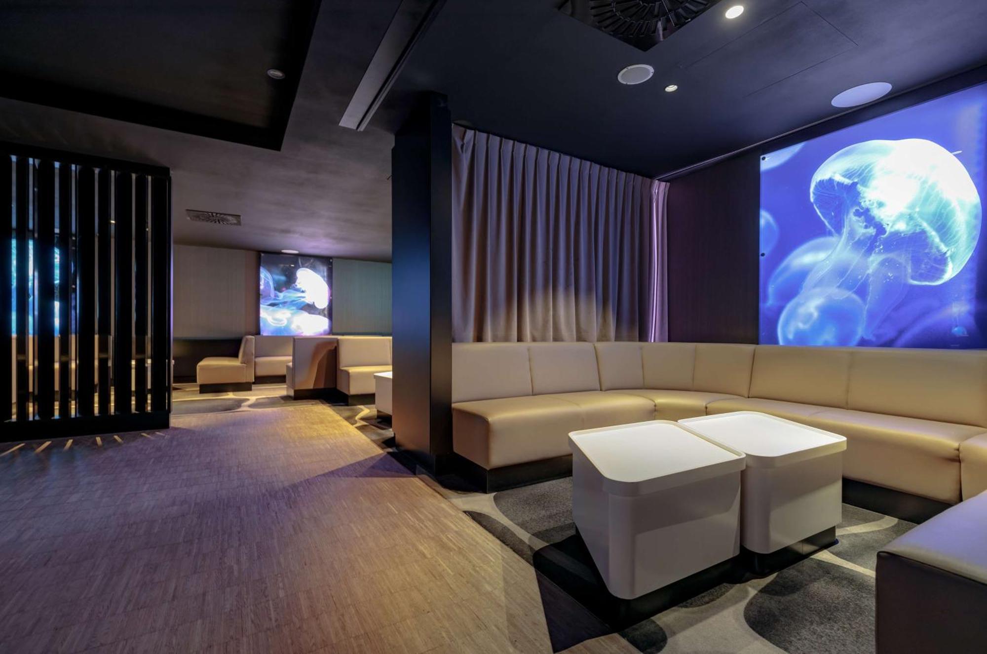 Radisson Blu Resort Swinoujscie Kültér fotó The photo shows a modern interior space that appears to be a lounge or relaxation area. The design is sleek and minimalist, featuring a curved, light-colored seating arrangement with low tables at the center. The walls are dark, contributing to a coz