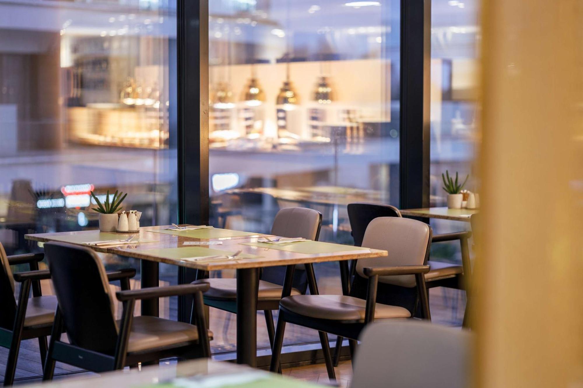 Radisson Blu Resort Swinoujscie Kültér fotó The photo shows a modern restaurant interior featuring several tables and chairs arranged under large windows. The tables are set with green placemats and cutlery. There are small potted plants on the tables, adding a touch of decor. In the backgroun