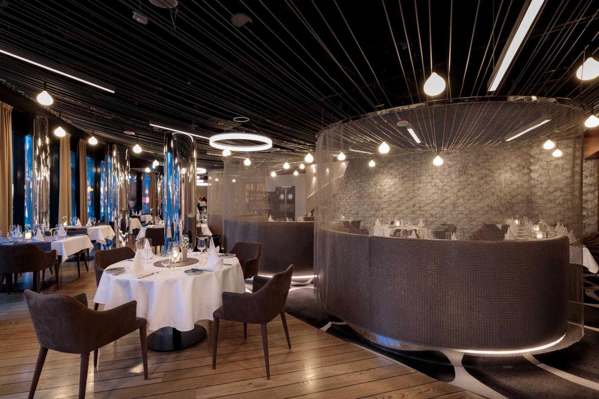 Radisson Blu Resort Swinoujscie Kültér fotó The photo shows an elegant restaurant interior. It features polished wooden floors and contemporary decor. Round tables are set with white tablecloths and have chairs arranged around them. The lighting is modern, with multiple pendant lights hanging 