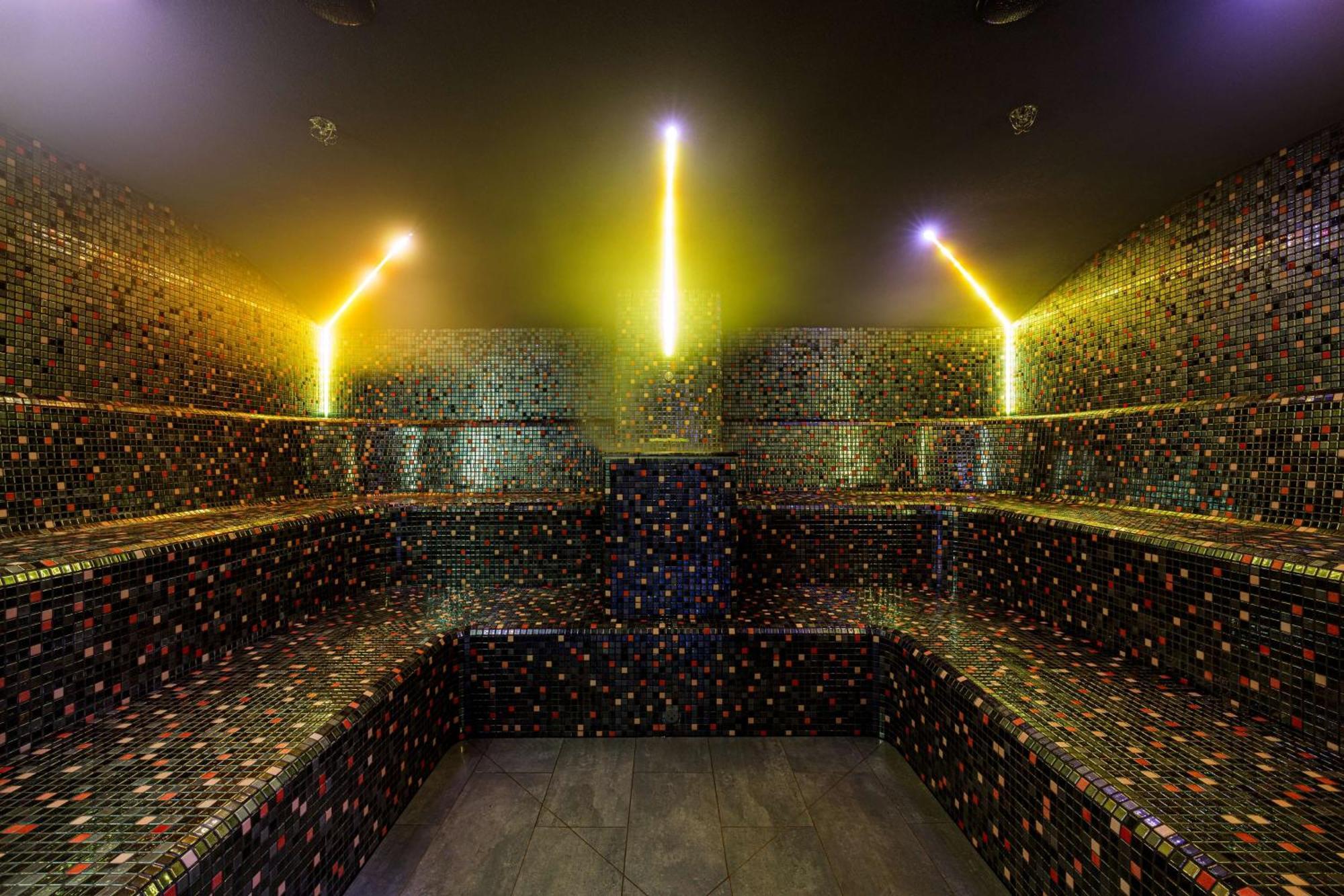 Radisson Blu Resort Swinoujscie Kültér fotó The photo shows the interior of a steam room or sauna. The space is characterized by a series of benches that are built into the walls, allowing for multiple seating options. The walls are adorned with a mosaic of small, colorful tiles that create a 