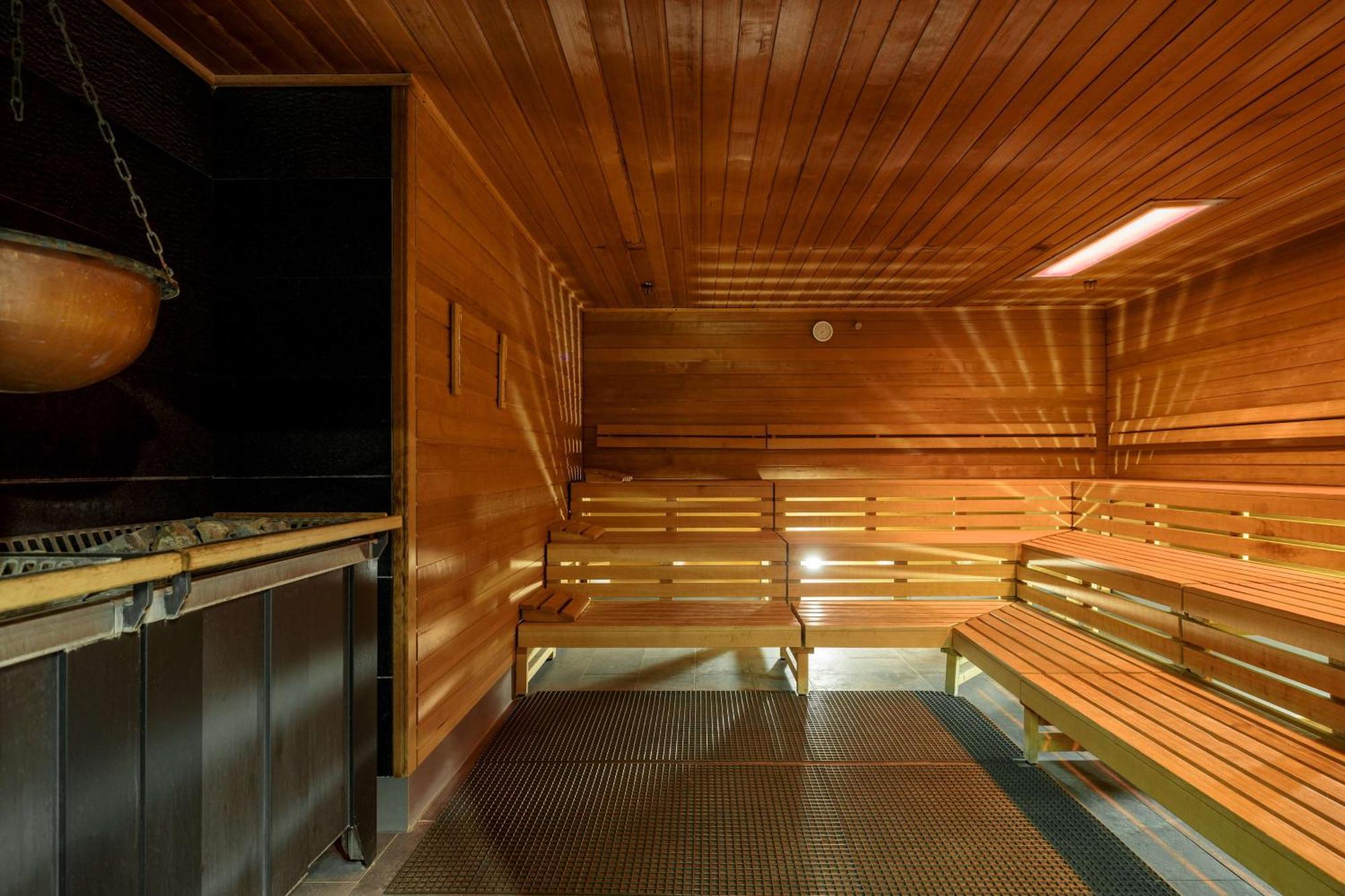 Radisson Blu Resort Swinoujscie Kültér fotó The photo shows the interior of a sauna. The walls and benches are made of wood, creating a warm and inviting atmosphere. There is a heater, likely for generating steam, and a metal rack connected to it, perhaps for holding stones or water. The desig