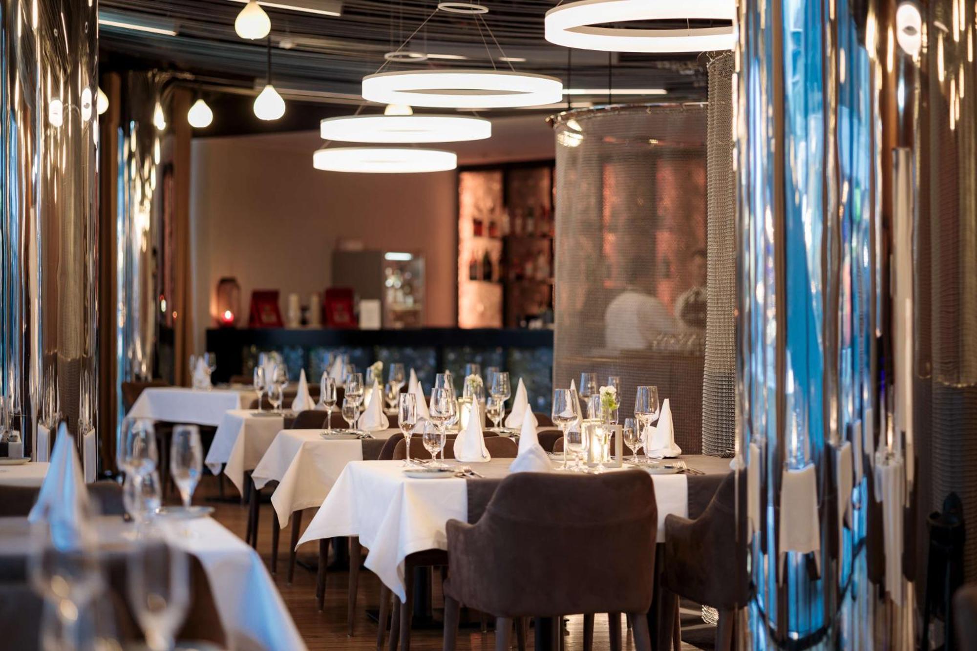 Radisson Blu Resort Swinoujscie Kültér fotó The photo depicts an elegant restaurant interior. There are several tables covered with white tablecloths, each set with glassware and napkins, suggesting a fine dining experience. The chairs are upholstered, providing a comfortable seating arrangeme