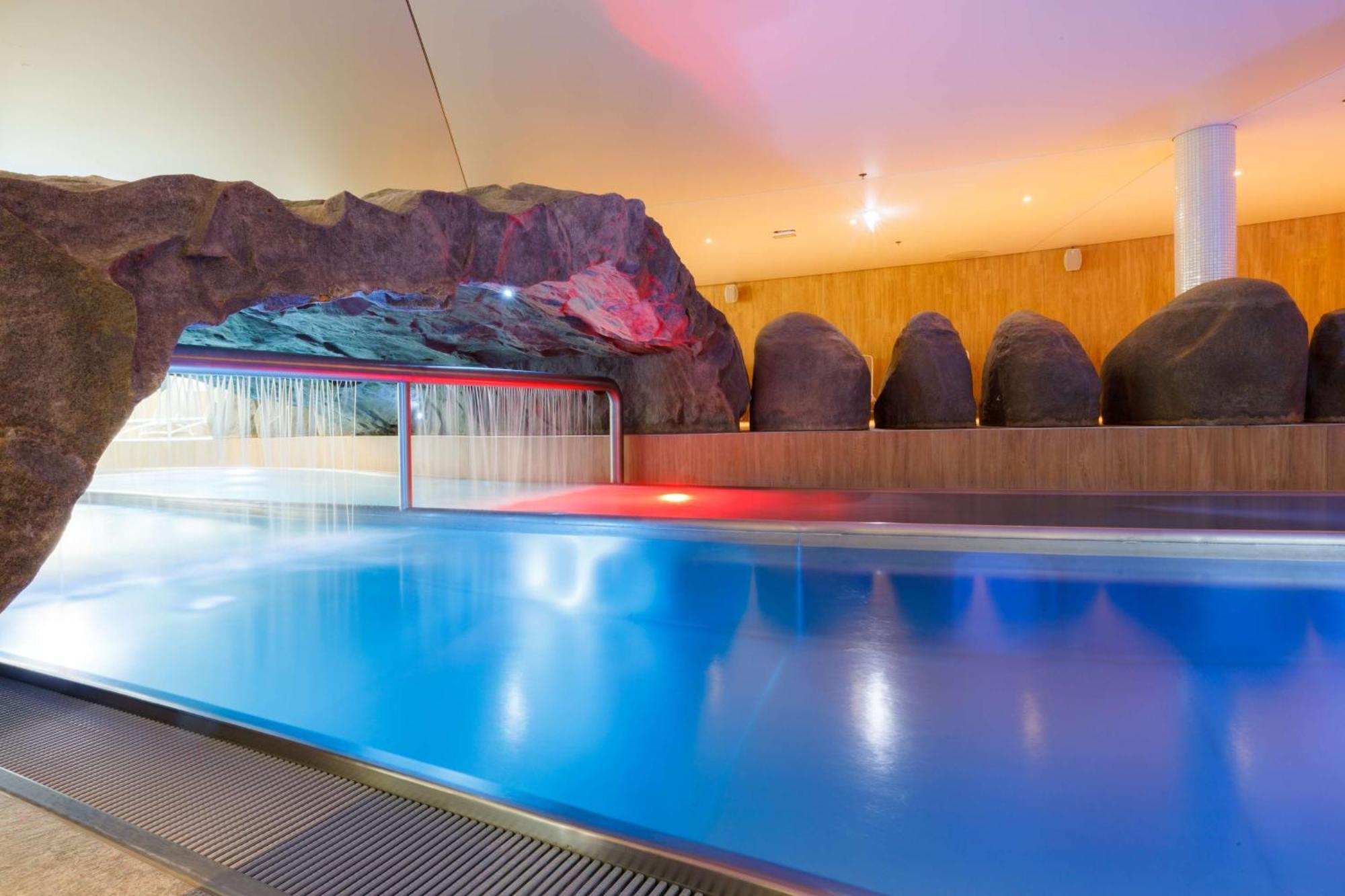 Radisson Blu Resort Swinoujscie Kültér fotó The photo shows a serene indoor swimming pool area. The pool has clear blue water, and there is a distinctive rock formation that resembles a cave on one side. Soft lighting enhances the atmosphere, casting a gentle glow across the space. In the back
