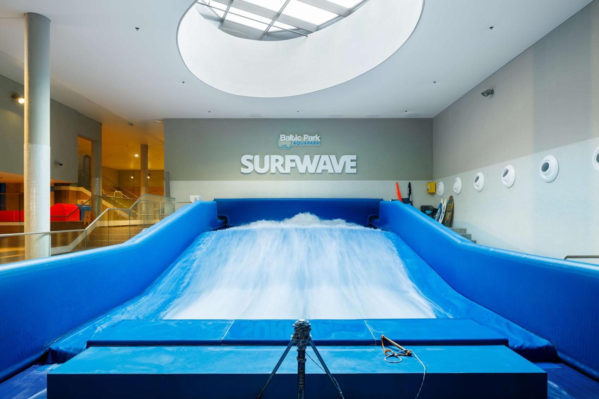 Radisson Blu Resort Swinoujscie Kültér fotó The photo shows an indoor surfing attraction called "Surfwave." It features a large blue ramp with water flowing down it, creating a wave-like effect for surfing. Above the ramp, there is a sign that says "SURFWAVE." The area appears well-lit and mod